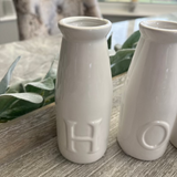 Two white ceramic vases with 'H' and 'O' on a wooden surface.
