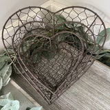 Decorative metal heart-shaped basket with greenery on a wooden surface