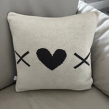 Decorative pillow with black heart and cross symbols on a light gray couch.