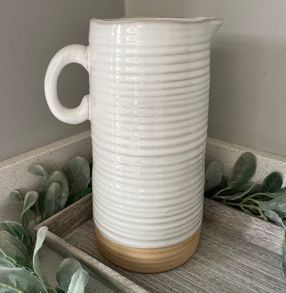 White ribbed ceramic pitcher on a wooden surface with greenery