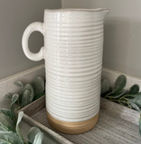 White ribbed ceramic pitcher on a wooden surface with greenery
