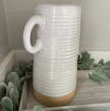 White ribbed ceramic vase on a wooden surface with greenery