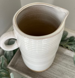White ceramic pitcher with a handle on a surface with greenery