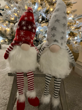 Two Christmas-themed gnomes on a stand with a decorated tree in the background.