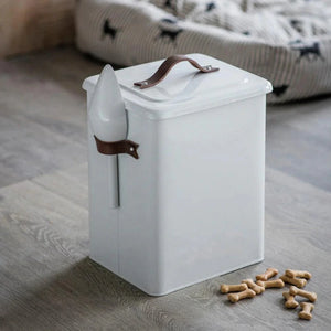 White pet food container with a lid on a wooden floor next to scattered dog treats.
